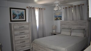 Una camera da letto con un letto di legno, una cassettiera, una ventola a soffitto e due quadri alle pareti.