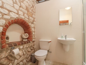 A bathroom with a stone wall, a toilet, a sink, and a mirror.