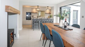 A modern kitchen with a central island, built-in oven, and a wood-burning stove. - Ty Bara (Cemaes Bay)