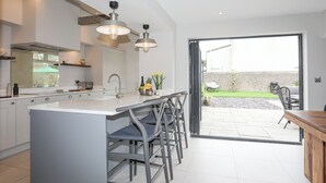 A modern kitchen with a central island, bar stools, and a view of the outdoor patio area. - Ty Bara (Cemaes Bay)