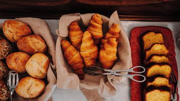 A variety of baked goods including bread rolls, croissants, and a loaf of cake on a table.