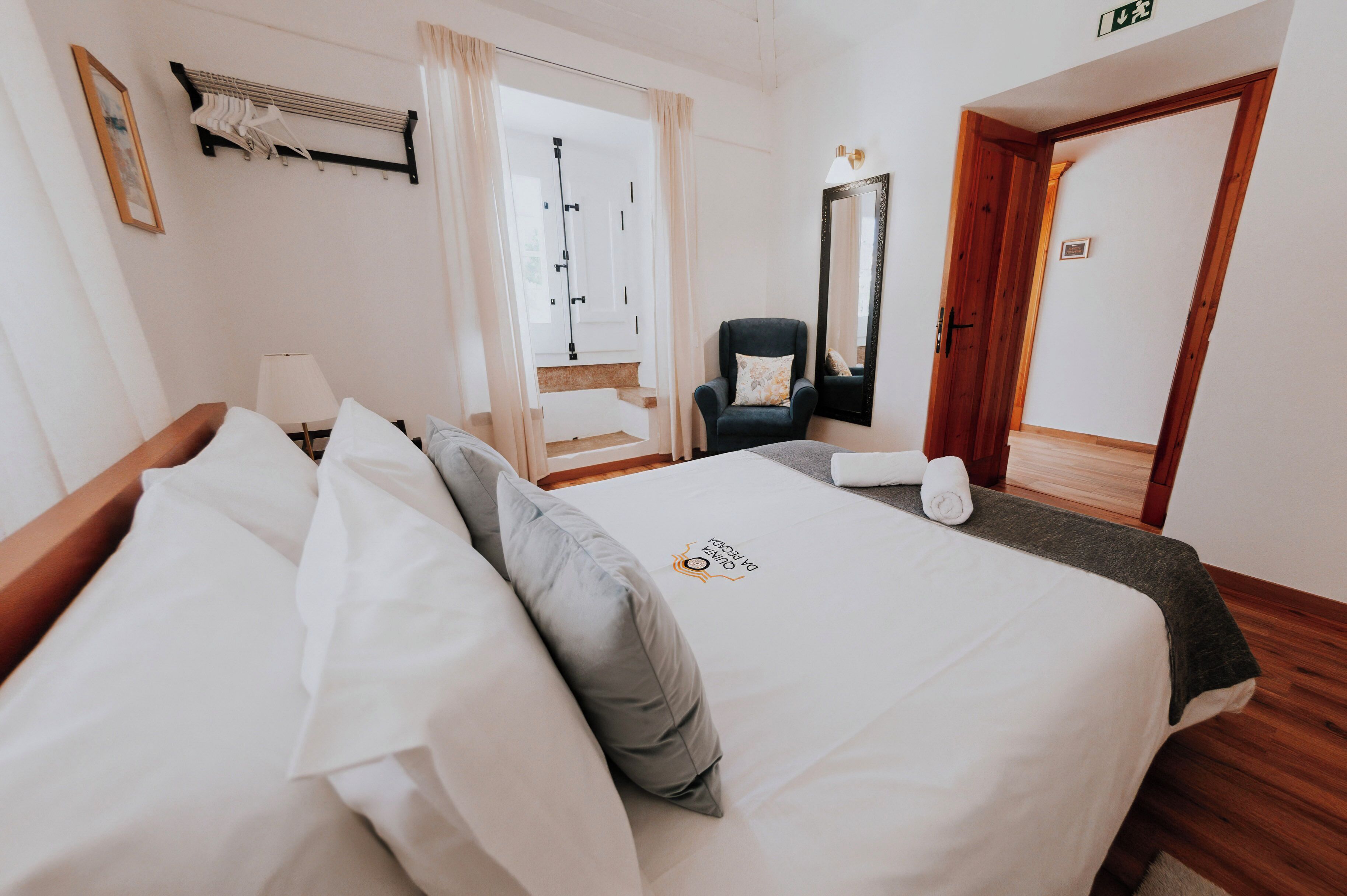 A hotel room with a bed, a chair, a mirror, and a door.