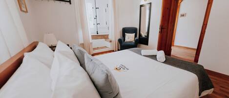 A hotel room with a bed, a chair, a mirror, and a door.