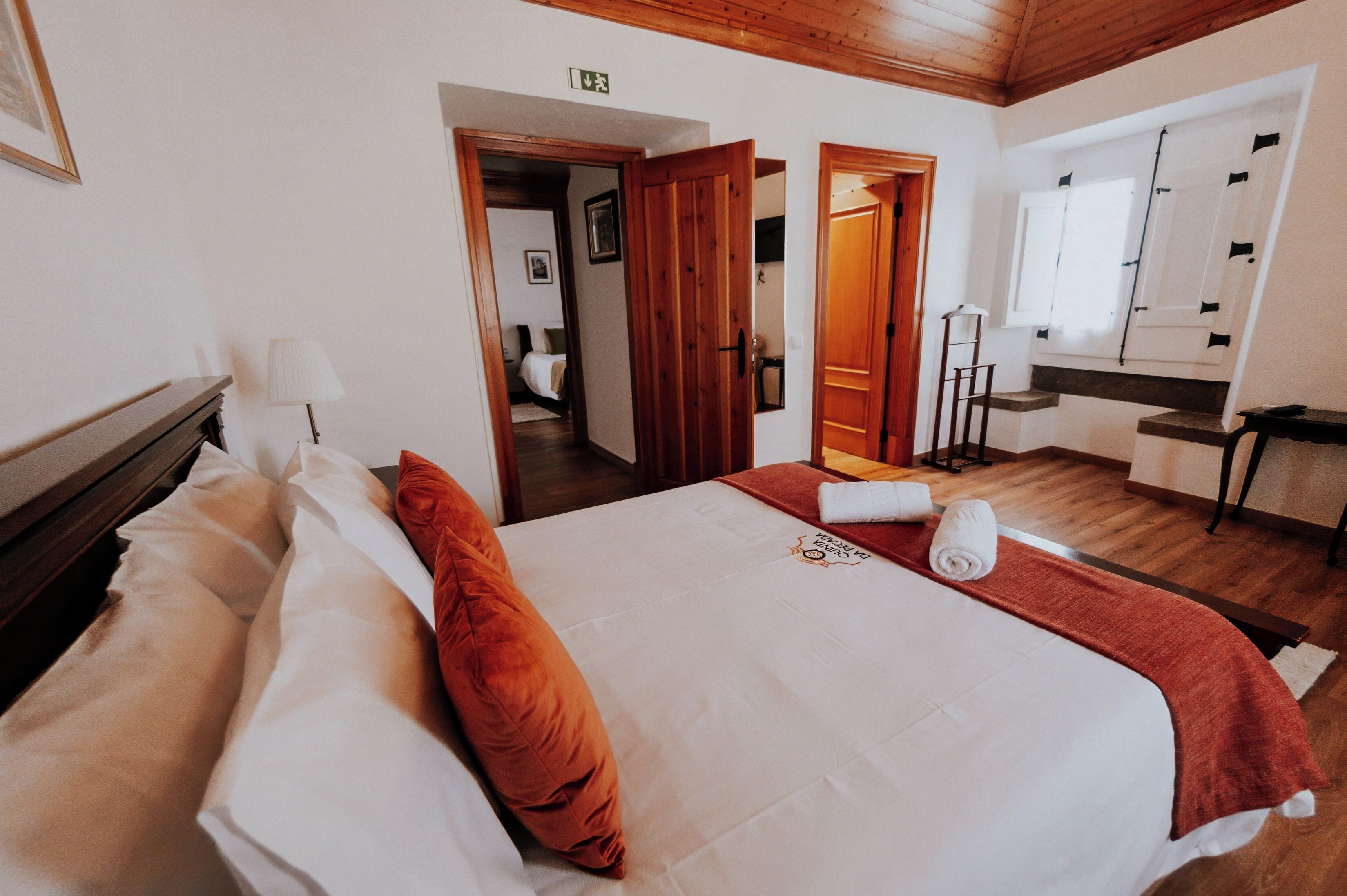 Una habitación de hotel con una cama, cabecera de madera, un espejo y una ventana con persianas.