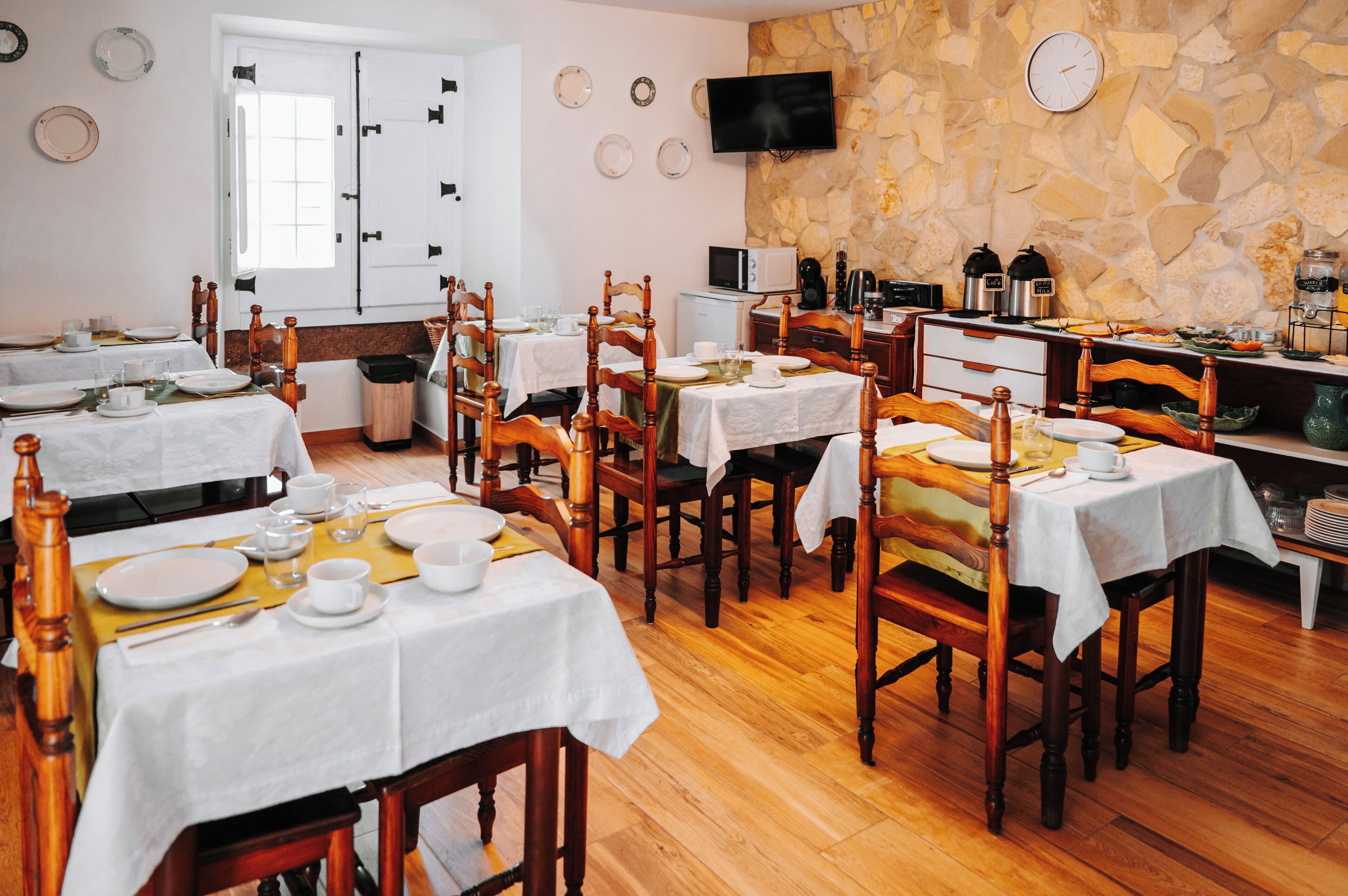A dining area with multiple tables, chairs, a stone wall, a television, and a clock.