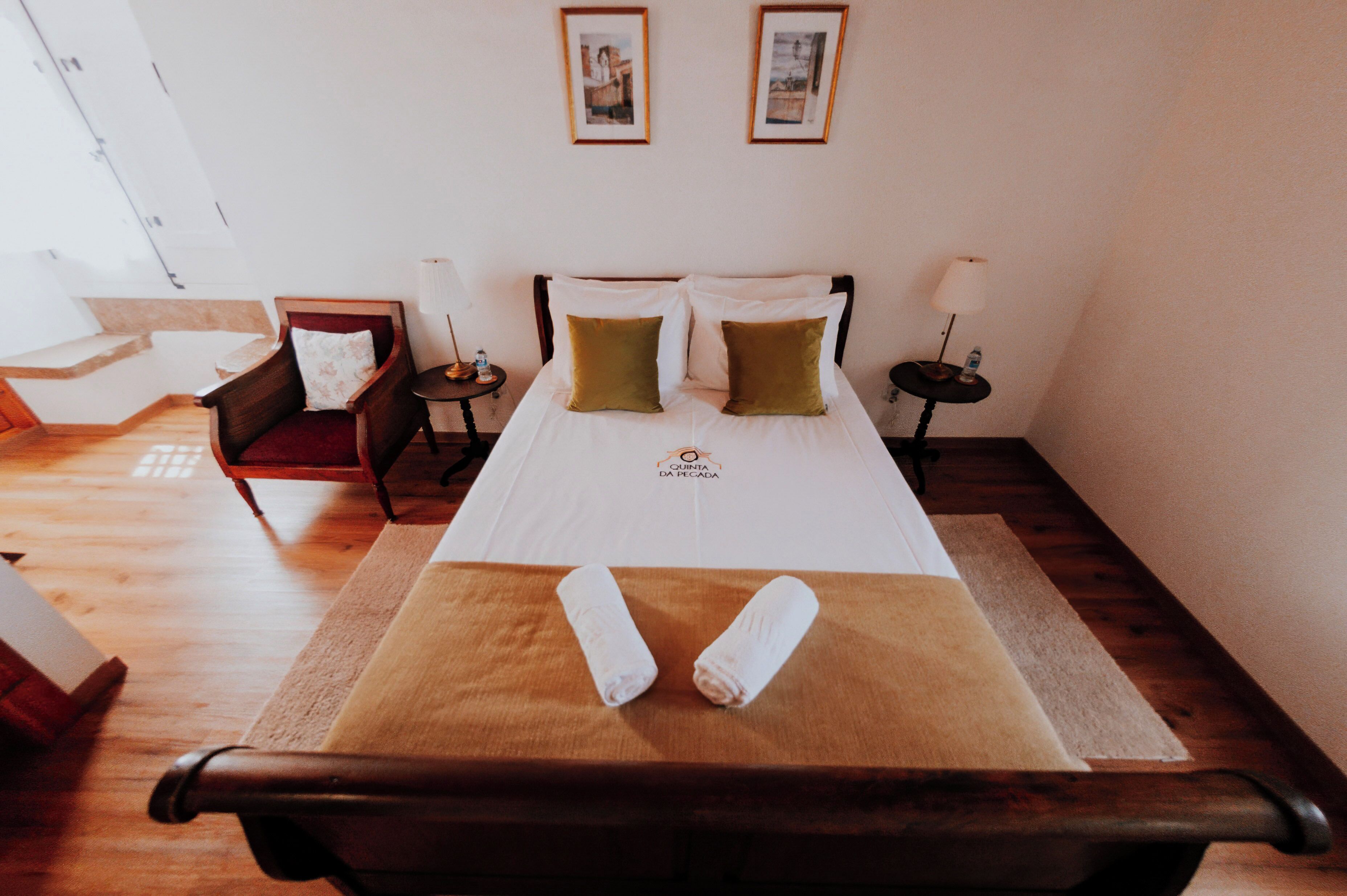 Una habitación de hotel con cama, una silla, una mesita de noche y un cuadro colgado en la pared.