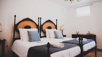 Two double beds with dark wooden frames and woven headboards, dressed in white linens and blue pillows.