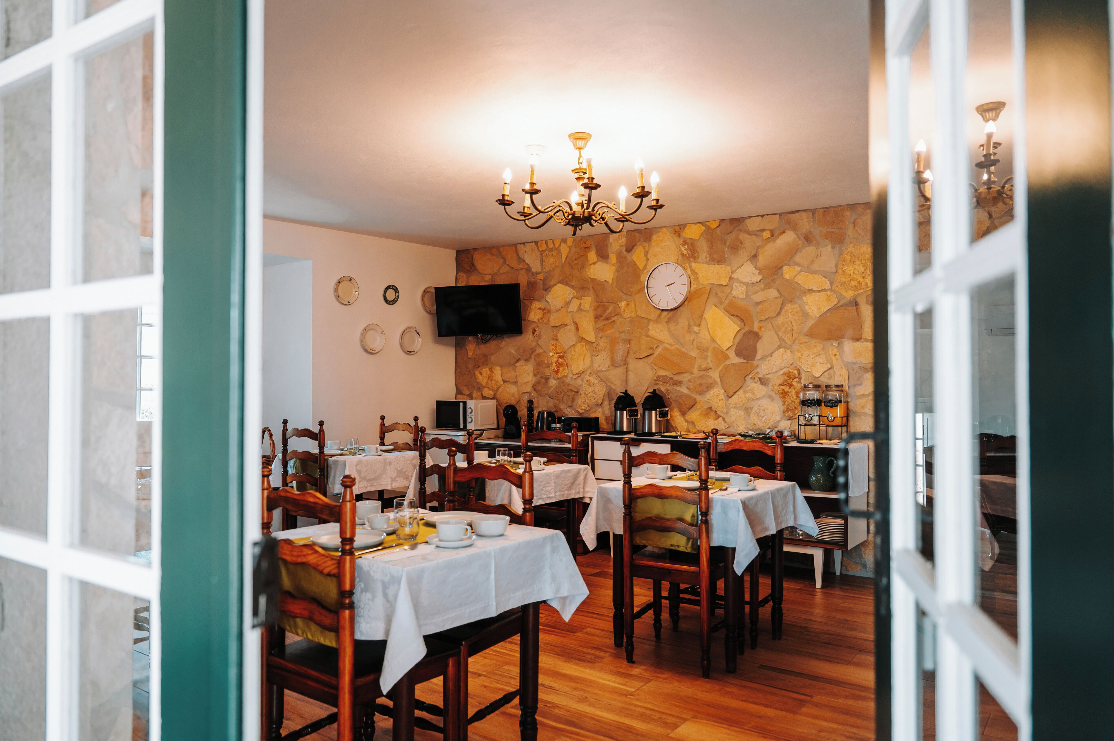 A dining area with wooden tables, chairs, a stone wall, a chandelier, and a flat-screen TV.
