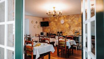 A dining area with wooden tables, chairs, a stone wall, a chandelier, and a flat-screen TV.