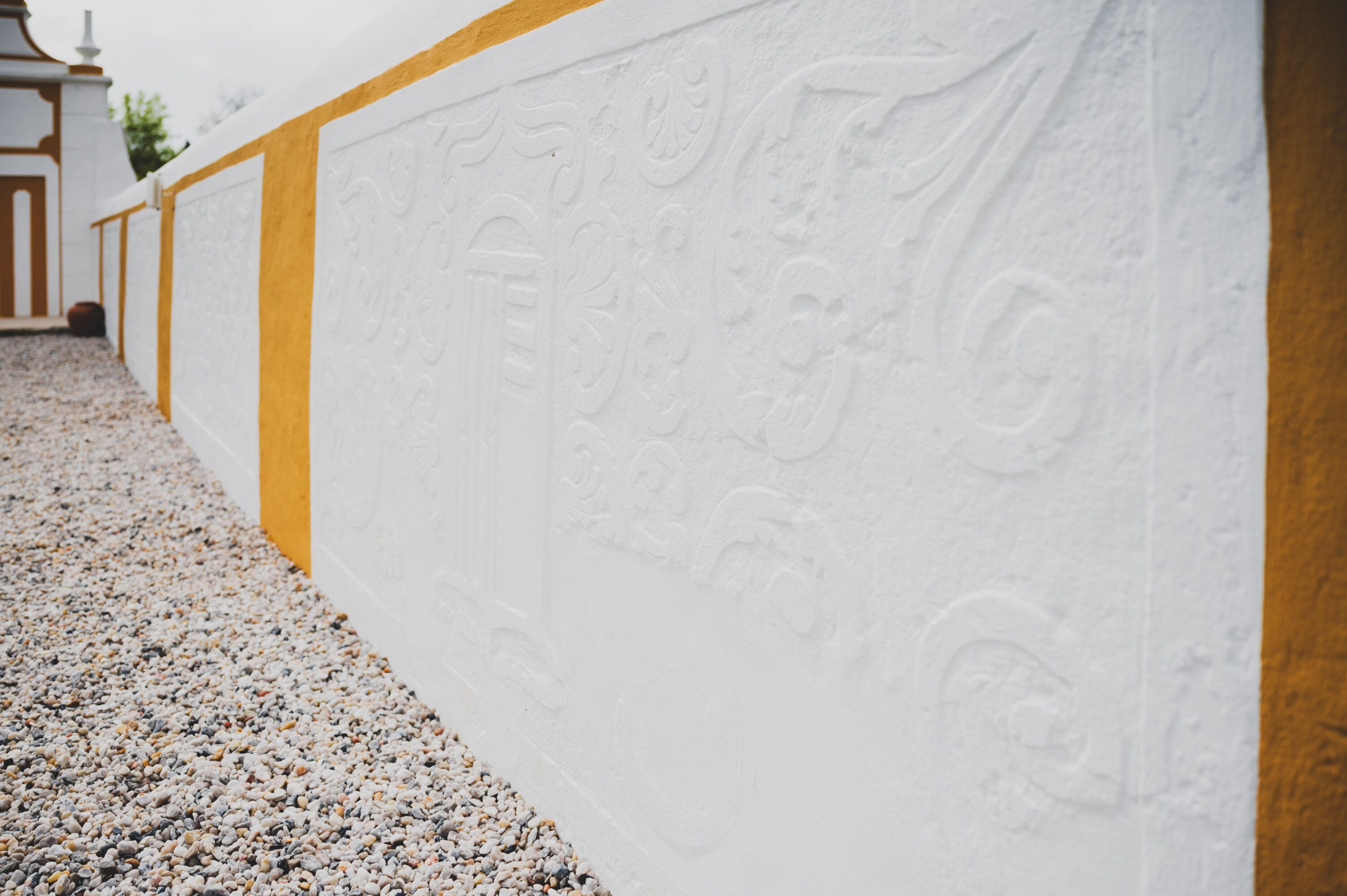Pared blanca con diseños decorativos en relieve y una franja vertical amarilla.