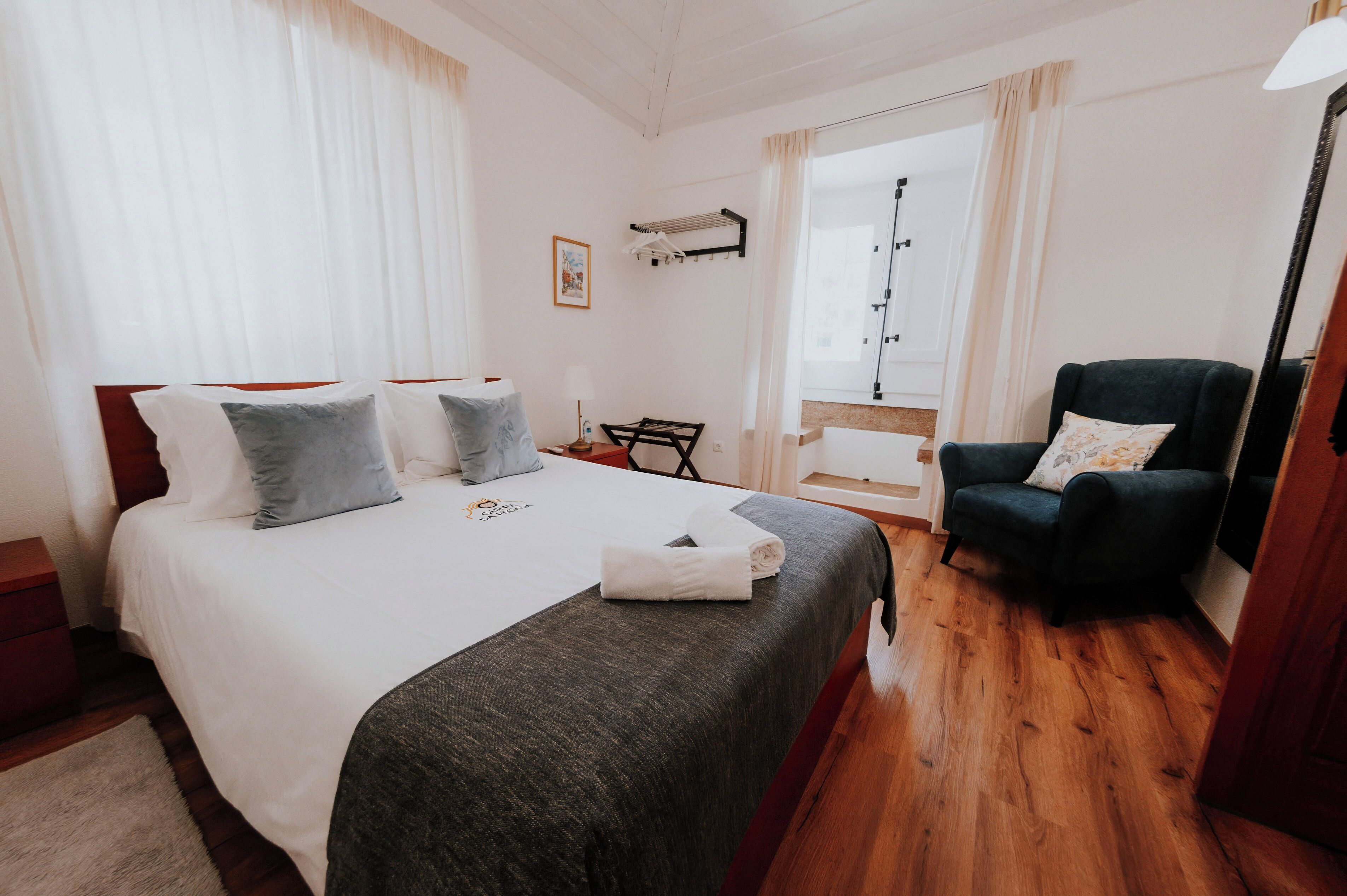 Una habitación de hotel con cama, una silla, un escritorio y un ventanal con cortinas.