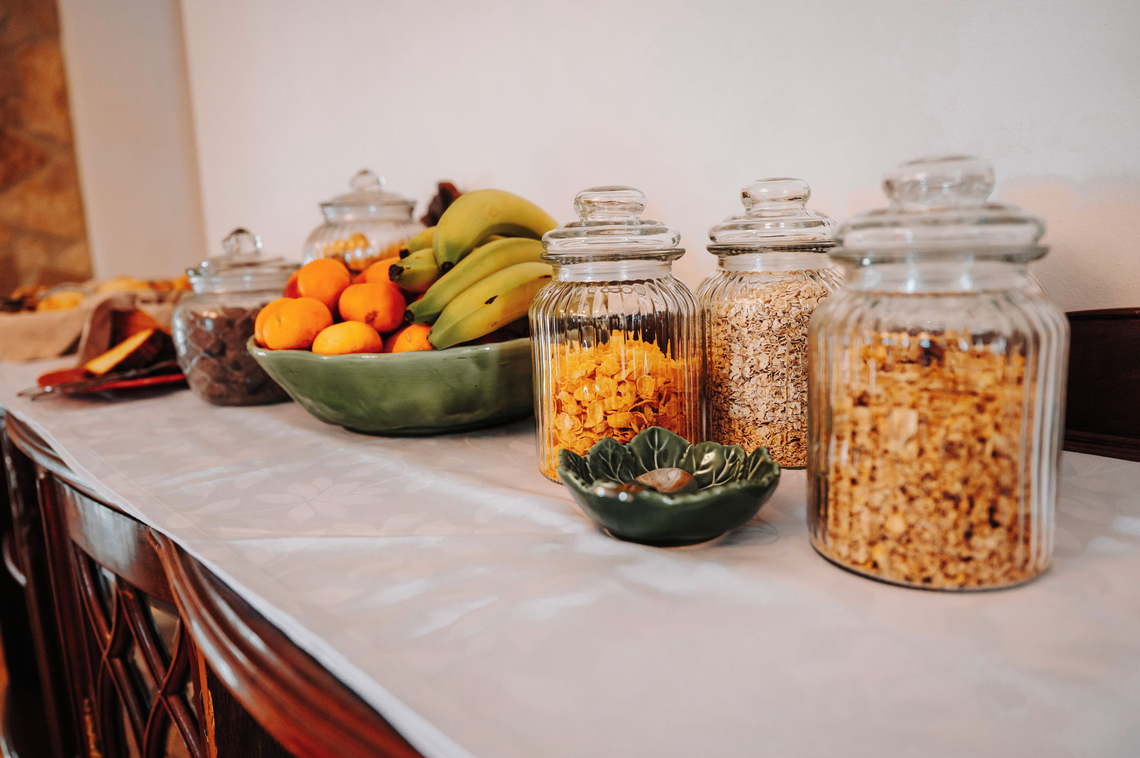 Una mesa de buffet con diferentes alimentos en recipientes de vidrio y un bol de frutas.