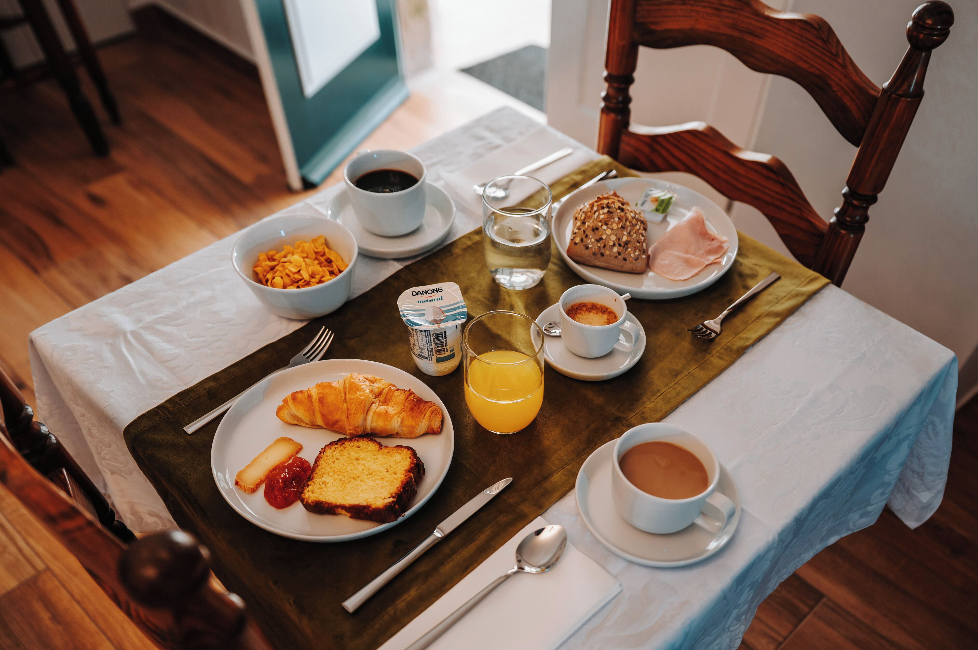 Une table de petit-déjeuner avec des croissants, des céréales, du café et du jus de fruits.