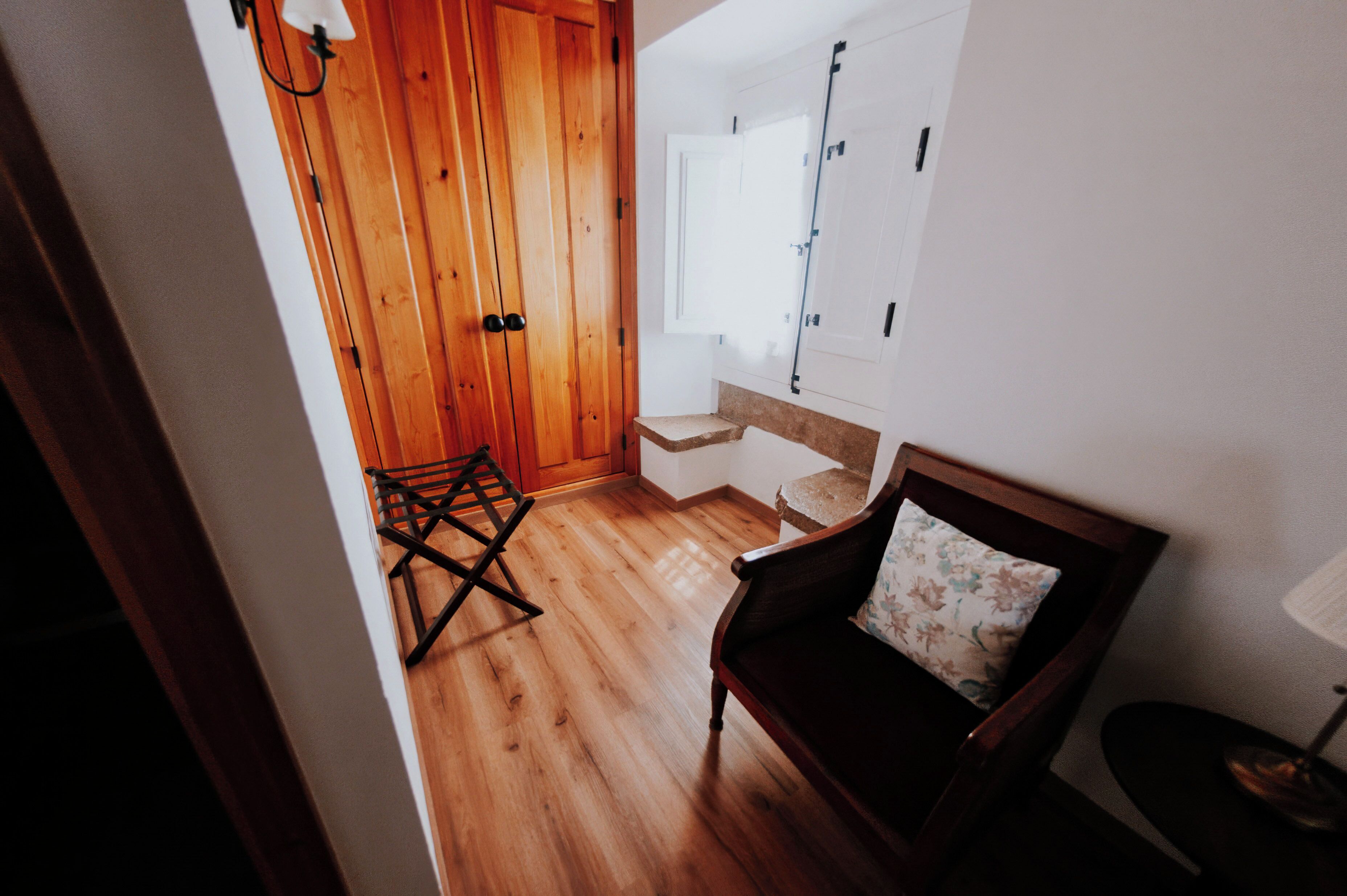 A wooden floor, a chair with a floral pillow, a small table, and a wall-mounted lamp.