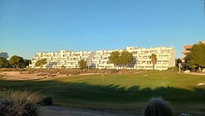 A modern building with multiple floors, likely a hotel or apartment complex, with a well-maintained lawn in the foreground.