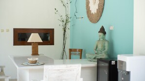 Ein Zimmer mit einem Holztisch, einer Lampe, einer Buddha-Statue, einem Stuhl und einem Fernseher.
