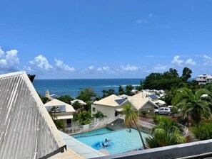 Relax by the resort's pool surrounded by lush greenery and palm trees, offering a view of the ocean.