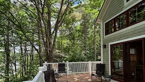 A covered deck with outdoor furniture, surrounded by trees.