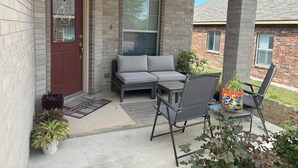 A covered porch with a red door, a gray sofa, and a metal chair. - Cozy 4-bedroom house in delightful San Antonio with AC, WiFi (San Antonio)