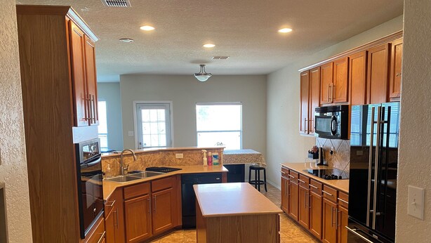 A kitchen with wooden cabinets, a central island, a microwave, and a refrigerator. - Cozy 4-bedroom house in delightful San Antonio with AC, WiFi (San Antonio)
