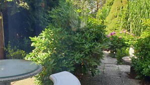 A garden pathway with a white stone bench and a table, surrounded by lush greenery and a neatly trimmed hedge. - Ferienwohnung in Alleinnutzung mit Garten und Teich, Nähe Sankt Peter Ording (Lehe)