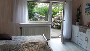 A bedroom with a bed, a window with curtains, a radiator, a dresser, and a potted plant. - Ferienwohnung in Alleinnutzung mit Garten und Teich, Nähe Sankt Peter Ording (Lehe)