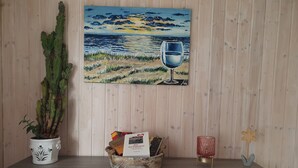 A wooden wall with a painting of a sunset and a glass of wine, a cactus plant, a decorative bowl, and a candle holder. - Ferienwohnung in Alleinnutzung mit Garten und Teich, Nähe Sankt Peter Ording (Lehe)