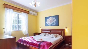 Ein Schlafzimmer mit einem hölzernen Bett, einem großen Fenster mit Vorhängen, einem Bild an der Wand und einem Nachttisch.