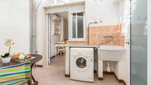 A compact kitchen with a washing machine, sink, and a dining area with chairs and a table. - Le Conchiglie - Monolocale by BarbarHouse (Maruggio)