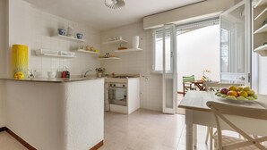 A kitchen with white cabinetry, a central island, and a dining area with a table and chairs. - Le Conchiglie - Monolocale by BarbarHouse (Maruggio)