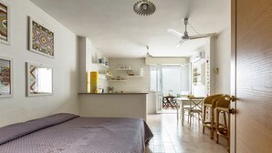 A bedroom with a bed, a kitchenette, and a dining area with chairs. - Le Conchiglie - Monolocale by BarbarHouse (Maruggio)