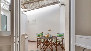 A dining area with a round table and four chairs, a small vase with flowers, and a window with blinds. - Le Conchiglie - Monolocale by BarbarHouse (Maruggio)