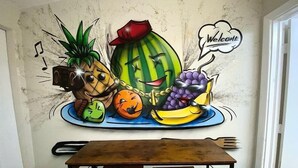 A mural of a watermelon with a red hat, a pineapple, a pumpkin, and grapes on a plate, with a 'Welcome' sign above.