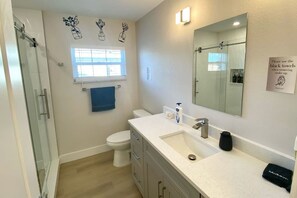 A modern bathroom with a glass shower enclosure, a white toilet, a sink with a mirror, and a towel rack. - Gulf Gateway-Pool/Dock/Grill/Fun (Fort Myers)