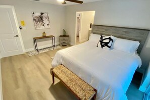 A bedroom with a bed, a bench, a bedside table, a small cabinet, and a painting on the wall. - Gulf Gateway-Pool/Dock/Grill/Fun (Fort Myers)