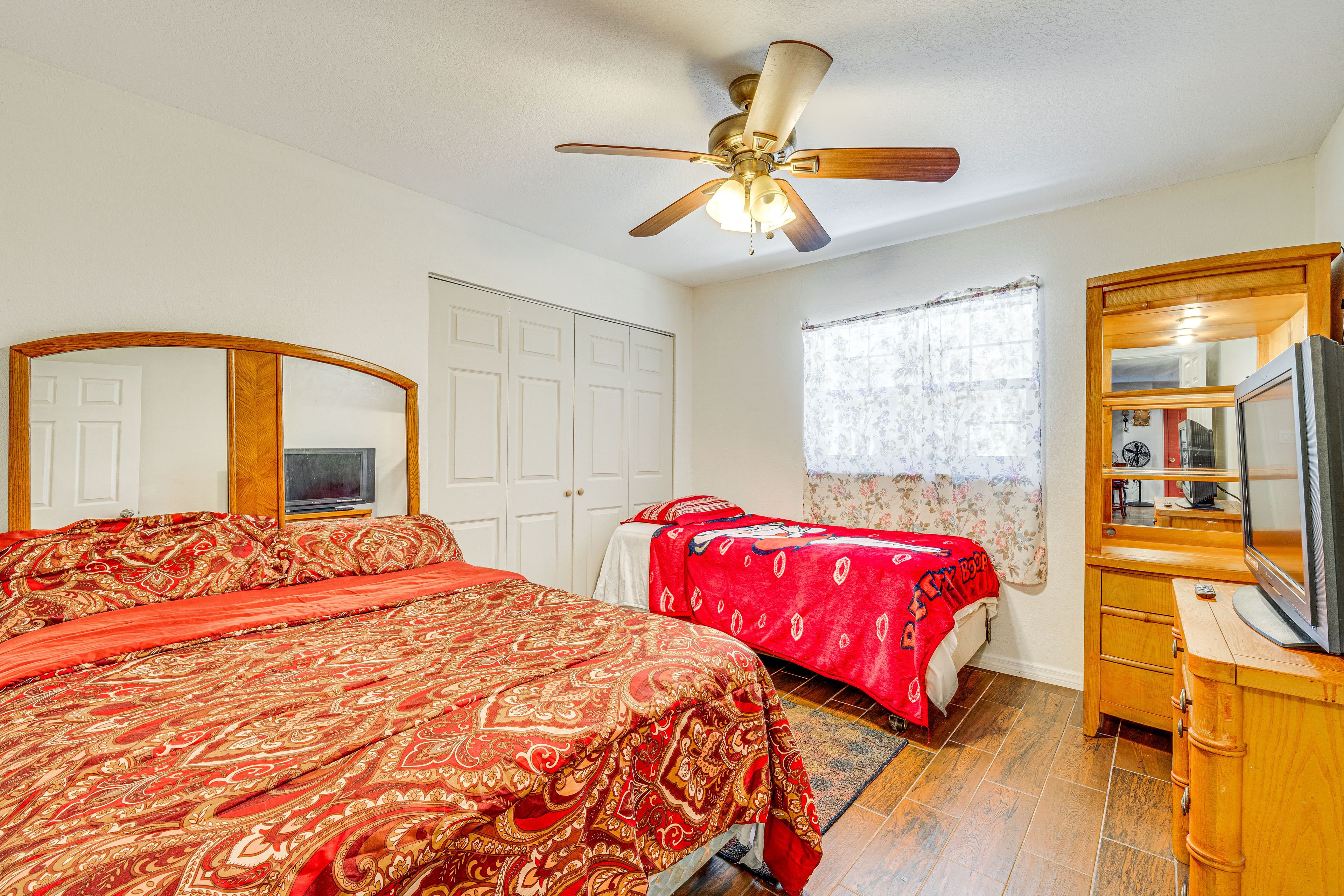 A bedroom with a large bed, a smaller bed, a ceiling fan, a wooden dresser, and a television.