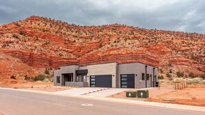 A modern two-story building with a flat roof, large windows, and a garage door. It is situated in a desert landscape with red rock formations in the background.