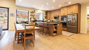 A modern kitchen with wooden cabinets, a central island, and a dining area with wooden chairs.