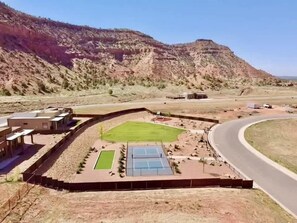 A sports complex with a tennis court, a basketball court, and a fenced area with a green field. - Luxury Kanab Home | Rooftop Stargazing & Views (Kanab)