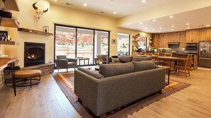 A spacious living area with a fireplace, a sofa, and a dining area with wooden cabinets and a kitchen in the background. - Luxury Kanab Home | Rooftop Stargazing & Views (Kanab)