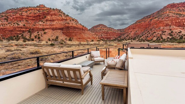 A rooftop terrace with a wooden deck, seating area, and a view of red rock formations.