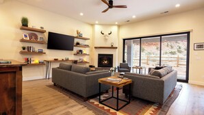 A living room with two sofas, a fireplace, a TV, and a large window with a view of a desert landscape.