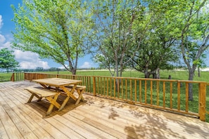 A wooden deck with picnic tables and a railing overlooking a grassy field. - Breathtaking Texas Hill Country Getaway on 10 Acres for Everyone - Sleeps 16 (Comfort)