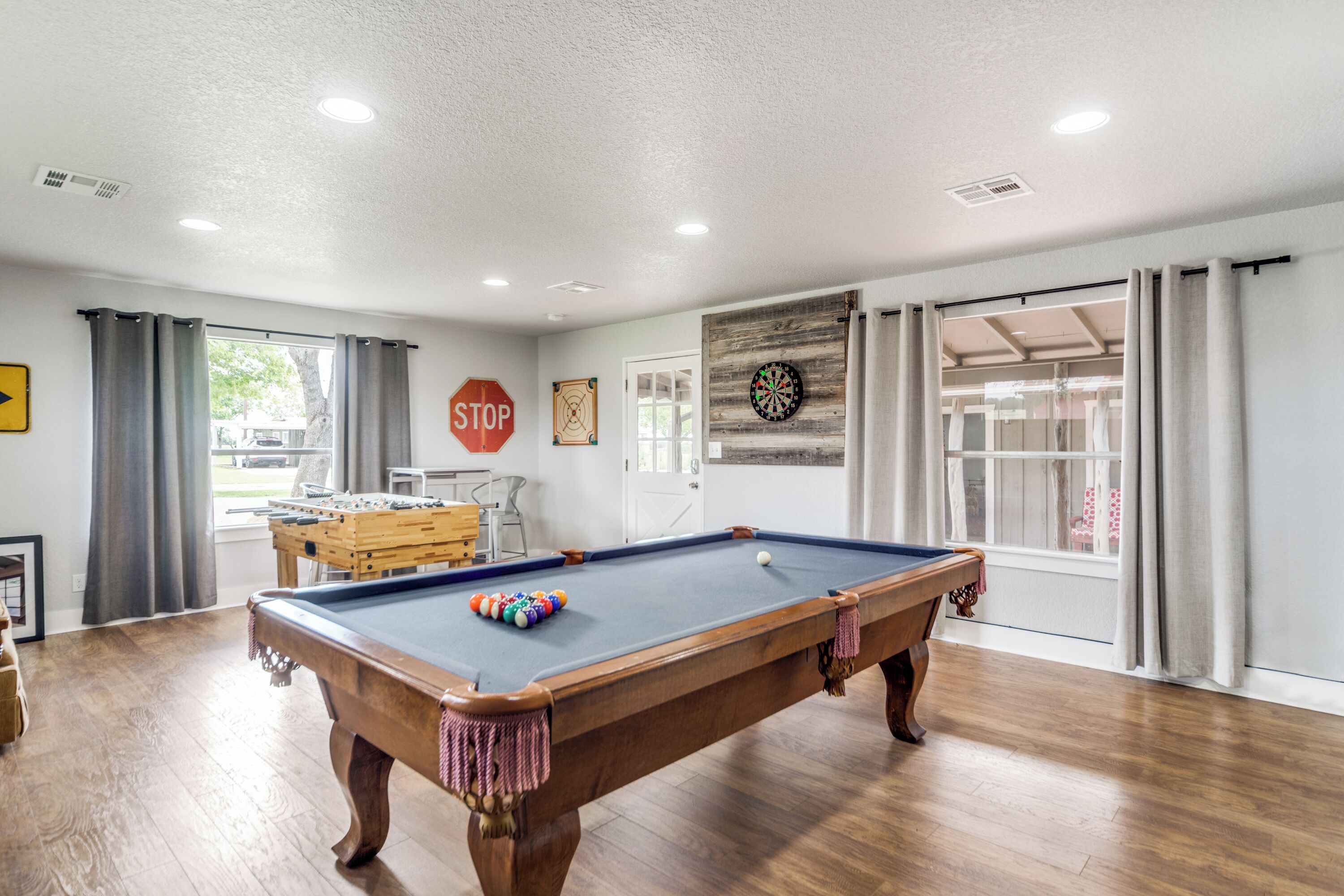 A pool table in a room with wooden flooring, a stop sign, and a dartboard on the wall.