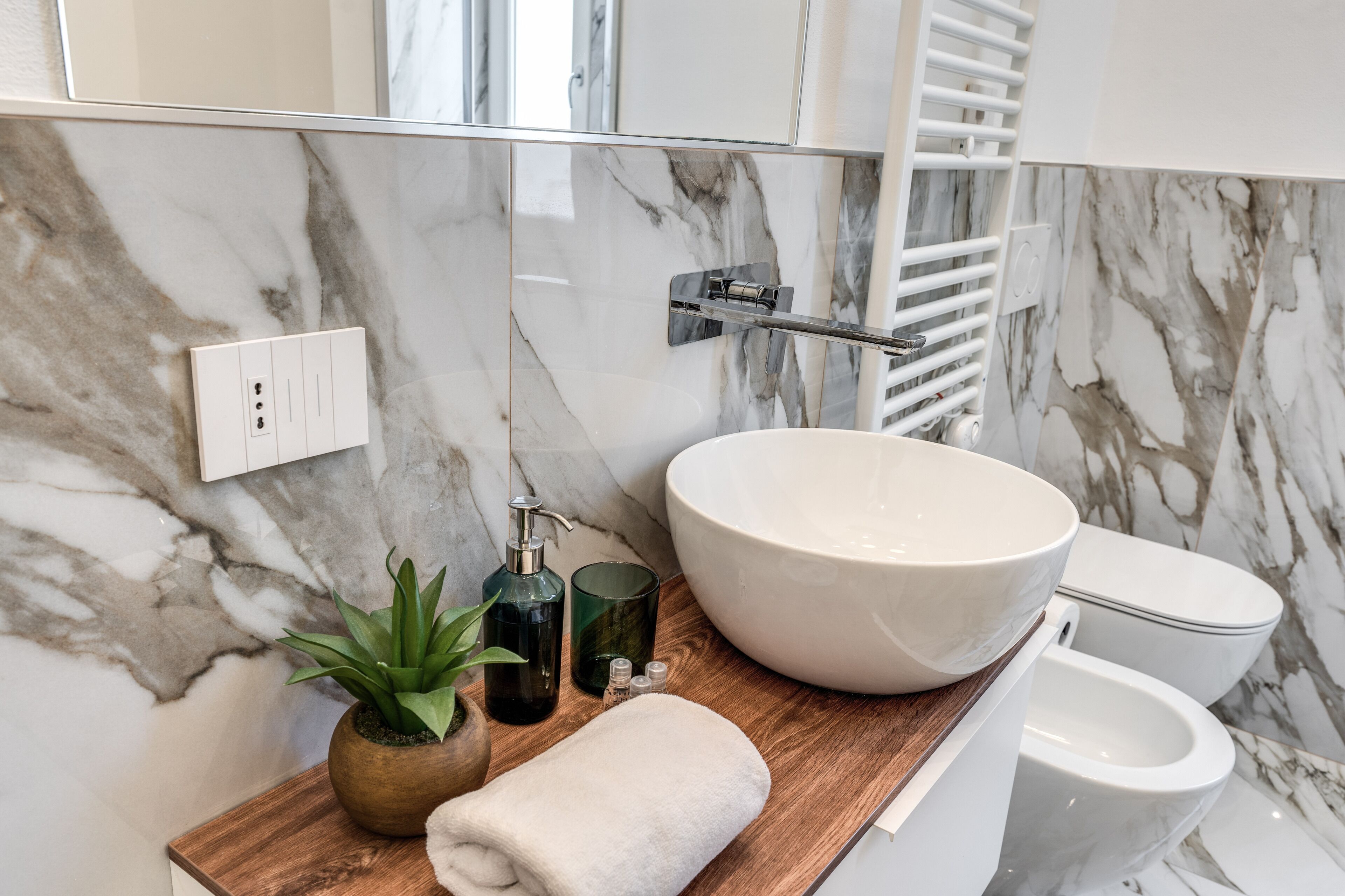A bathroom with a large marble sink, a wooden countertop, a potted plant, a towel, and a toilet.