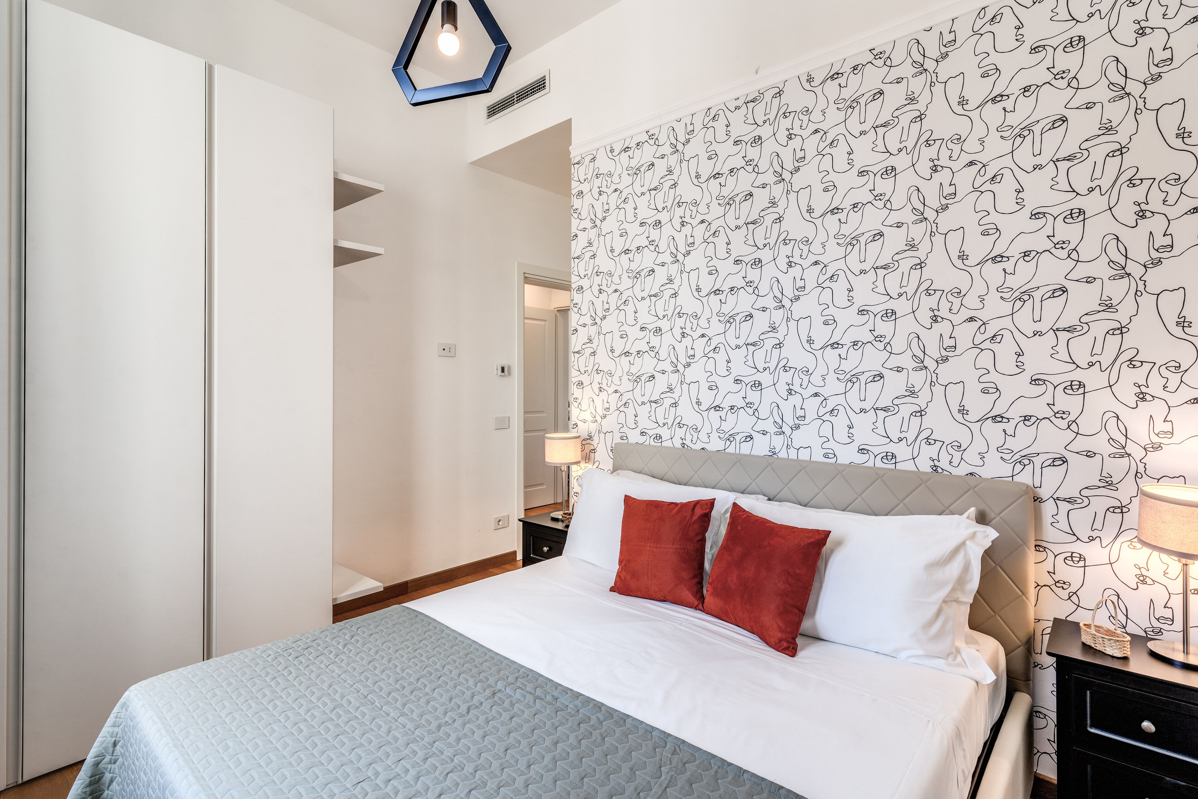 A bedroom with a bed, a nightstand, a lamp, and a wall with a pattern.