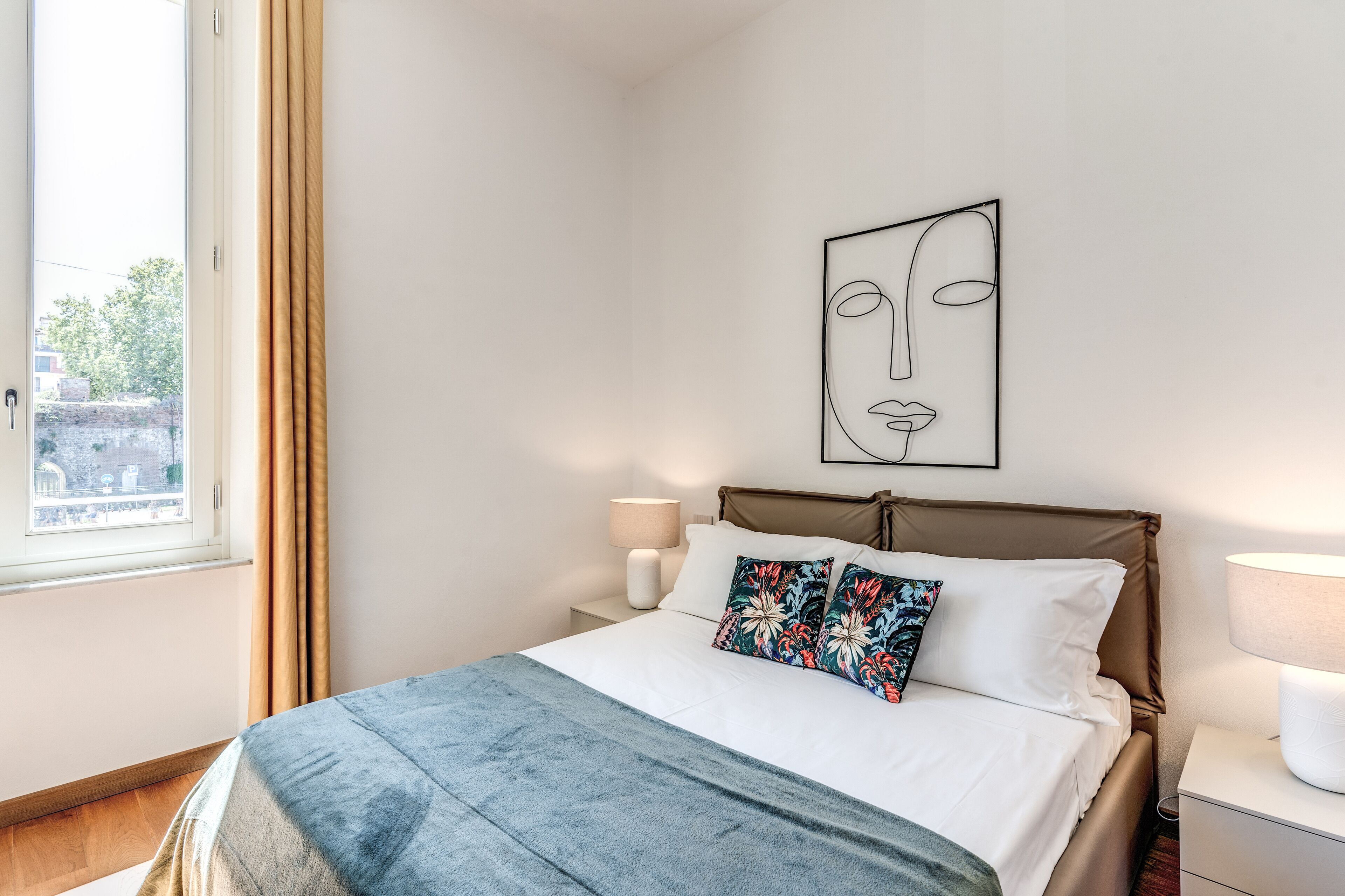 Una cama bien hecha con un edredón azul, una almohada colorida y una obra de arte minimalista en la pared.