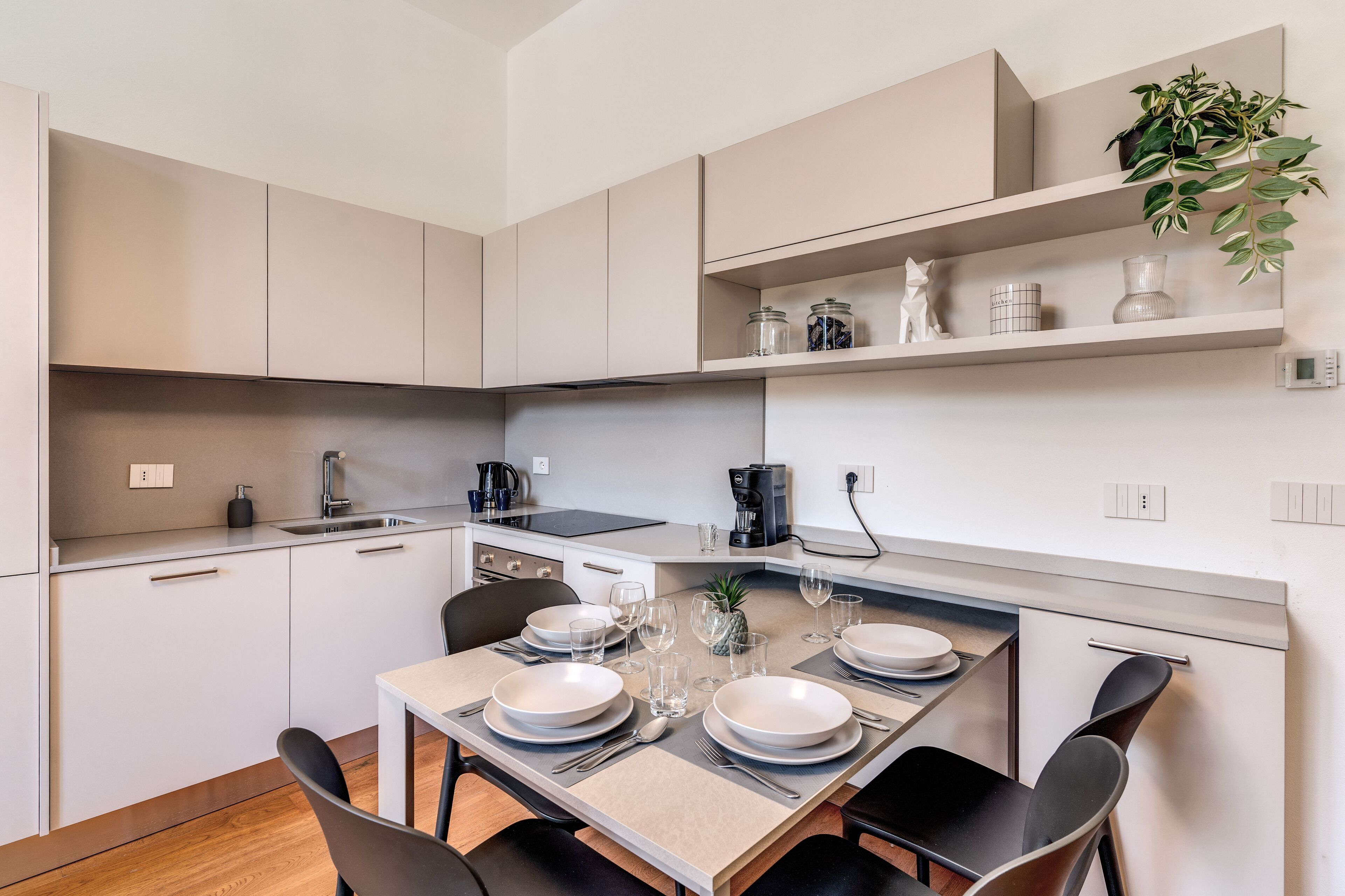 A modern kitchen with white cabinets, a dining table set for four, and a coffee machine.