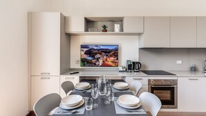 A modern kitchen with a dining area, featuring a flat-screen TV, stainless steel appliances, and a neatly set dining table with chairs. - AwesHome Luxury Apartment (Pisa)