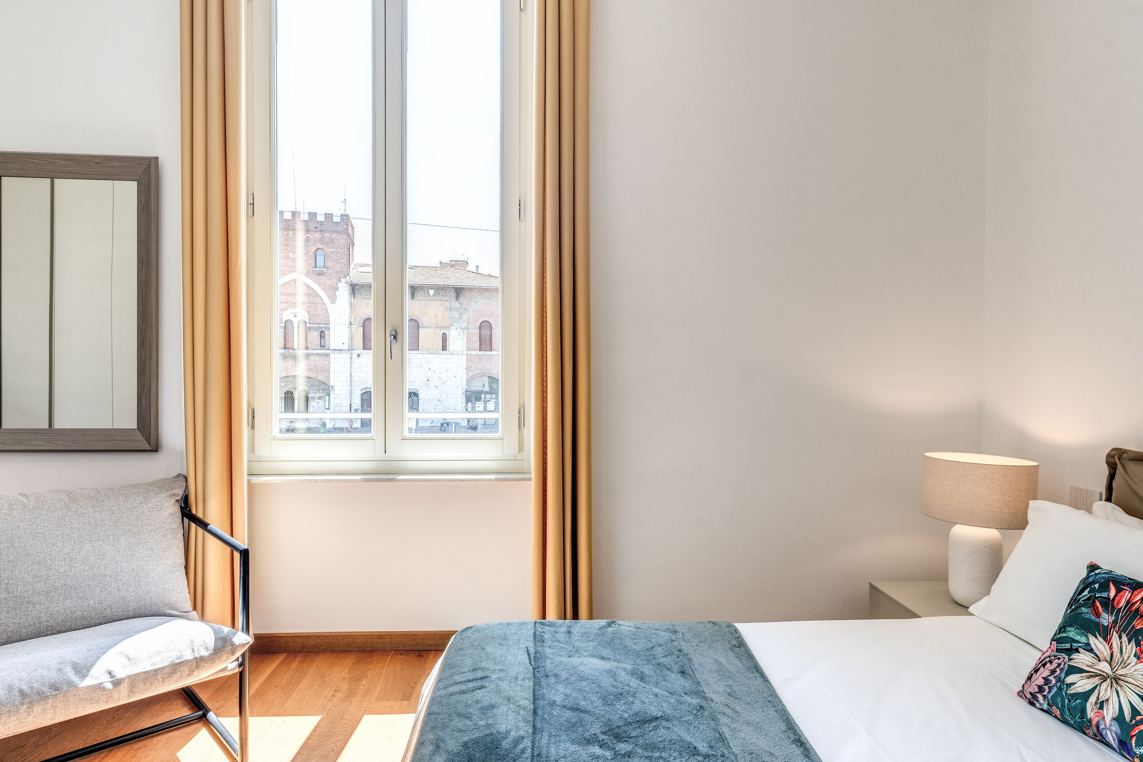 Un dormitorio con cama, mesita de noche, lámpara, silla y ventana con cortinas.
